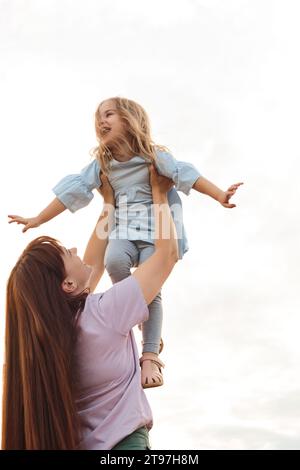 Madre felice che solleva la figlia sotto il cielo Foto Stock
