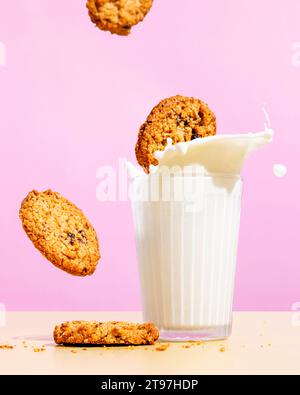 Biscotti farinata d'avena volanti vicino al latte che spruzza nel vetro su sfondo rosa Foto Stock