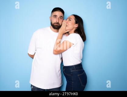 Bruna sussurra segreto al suo ragazzo su sfondo blu Foto Stock