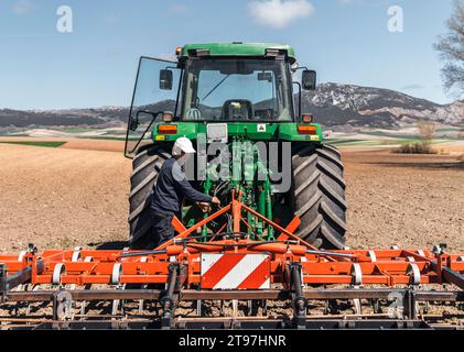 L'agricoltore regola l'aratro del trattore in piedi nel campo Foto Stock