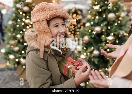 Madre con un bambino che tiene una confezione regalo vicino agli alberi di Natale Foto Stock