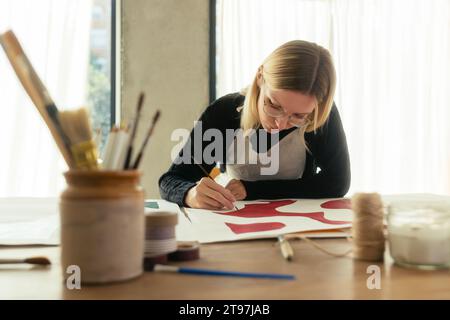 Artista biondo che dipinge su tela alla scrivania nello studio Foto Stock