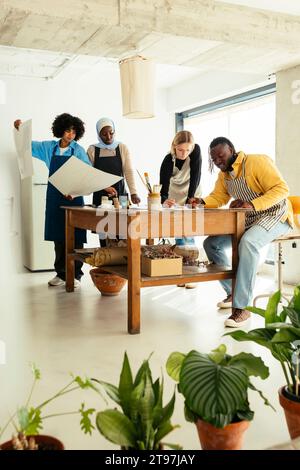 Artisti che confrontano dipinti e lavorano alla scrivania in studio Foto Stock