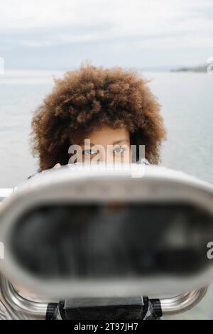 Donna con binocolo a gettoni davanti al lago Foto Stock