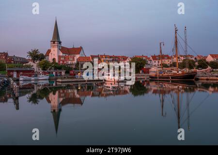 Danimarca, Bornholm, Ronne, Chiesa di San Nicola e case circostanti che si riflettono nell'acqua costiera al tramonto Foto Stock