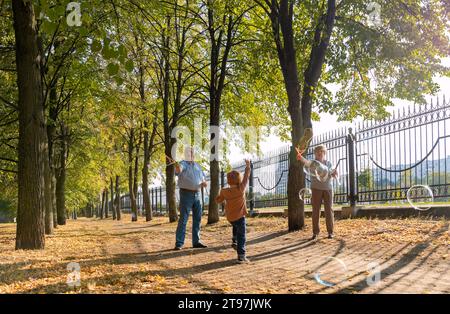 I nonni fanno bollicine e giocano con il nipote al parco nelle giornate di sole Foto Stock