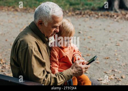 Nonno che mostra lo smartphone al nipote al parco Foto Stock