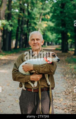 Un uomo anziano sorridente che tiene il cane Jack Russell Terrier in braccio al parco Foto Stock