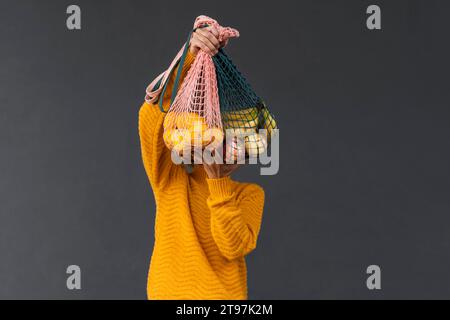 Donna che copre il viso con frutta in sacchetti in rete su sfondo nero Foto Stock