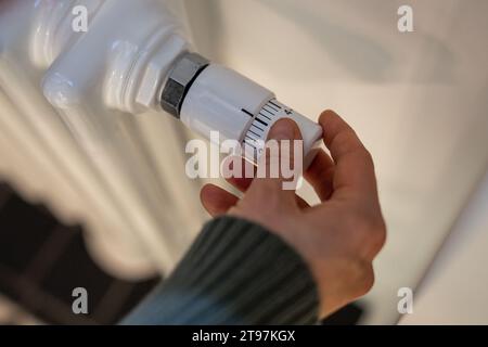 Donna regola il riscaldamento sul radiatore della batteria a casa durante la stagione fredda, con le mani in primo piano. Foto Stock