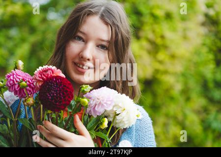 Adolescente sorridente che tiene fiori dahlia davanti alle piante Foto Stock