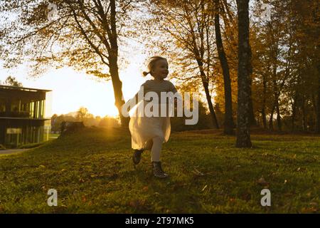 Ragazza felice che corre vicino agli alberi nel parco al tramonto Foto Stock