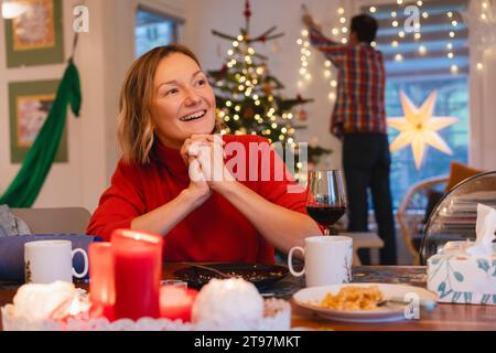 Donna felice con le mani stringate seduta a tavola durante le celebrazioni natalizie Foto Stock