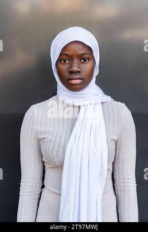 Giovane donna seria che indossa l'hijab davanti al muro Foto Stock