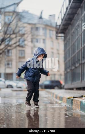 Un ragazzo carino che gioca sulla strada bagnata dopo la pioggia Foto Stock