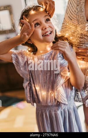 La madre regola la luce del filo sulla fronte della figlia a casa Foto Stock