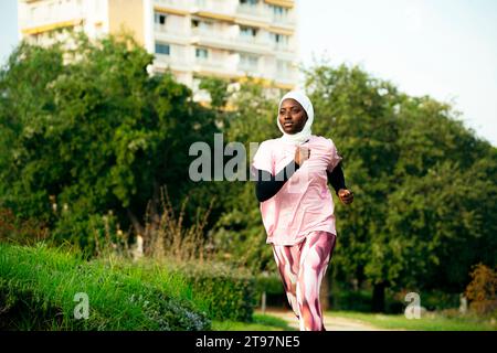 Giovane donna attiva che indossa hijab che corre nel parco Foto Stock