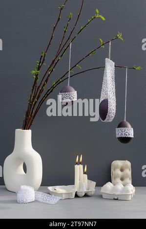 Foto studio di candele che bruciano sotto le uova di Pasqua allacciate appese ai ramoscelli in vaso Foto Stock