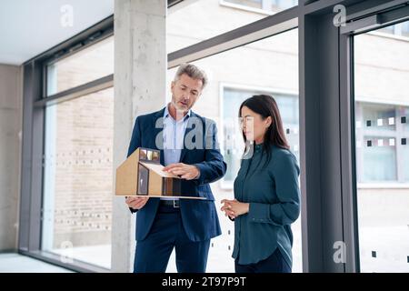 Architetto che discute con un collega sulla casa modello in ufficio Foto Stock