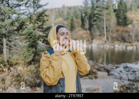 Donna che indossa una camicia con cappuccio e si trova vicino al fiume nella foresta Foto Stock