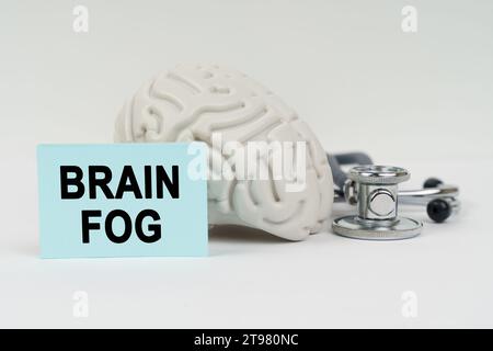 Concetto medico. Su una superficie bianca accanto al cervello c'è uno stetoscopio e adesivi con l'iscrizione - nebbia cerebrale Foto Stock