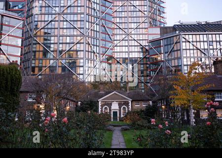 L'architettura moderna incombe su Hoptons Almshouses in Hopton Street, Southwark il 15 novembre 2023 a Londra, Regno Unito. Alti edifici in vetro si affacciano dietro queste case di importanza storica a Bankside e vicino alla Tate Modern. Fondata da Robert Hopton, pescivendolo nel 1730. Proprietà costruite intorno ad un giardino nel 1752 e sono ancora in uso. Prima dei giorni di provvigione statale per i vecchi, gli infermi o i poveri era comune per gli individui ricchi lasciare denaro o proprietà alla parrocchia locale o per istituire istituzioni indipendenti per assistere i bisognosi localmente.molte antiche parrocchie hanno tale isti Foto Stock