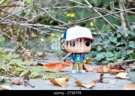 Funko Pop action figure di Dustin Henderson con bussola della famosa serie TV Netflix Stranger Things. Strada abbandonata, foresta autunnale, foglie. Foto Stock