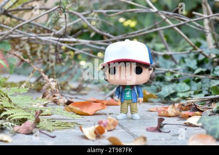 Funko Pop action figure di Dustin Henderson con bussola della famosa serie TV Netflix Stranger Things. Strada abbandonata, foresta autunnale, foglie. Foto Stock