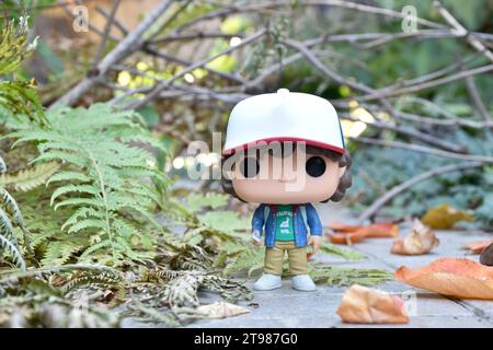 Funko Pop action figure di Dustin Henderson con bussola della famosa serie TV Netflix Stranger Things. Strada abbandonata, foresta autunnale, foglie. Foto Stock