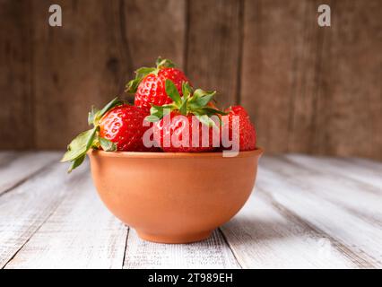 Fragole organiche grandi e succose mature in un recipiente di ceramica argillosa su fondo di legno. Foto Stock
