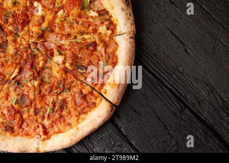 Pizza italiana con diversi tipi di carne su sfondo di legno nero, vista dall'alto, spazio per copiare. Foto Stock