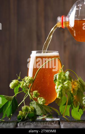La birra artigianale viene versata da una bottiglia in un bicchiere su uno sfondo di legno scuro. Birra e luppolo verde. Il concetto di birra naturale. Oktoberfest. Festival della birra. Foto Stock