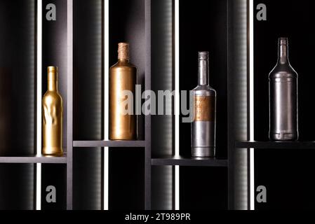 Una varietà di bottiglie di alcol, dipinte con vernice oro e argento, si stagliano su scaffali illuminati. Arredamento di un ristorante, bar, sala banchetti, bar Foto Stock