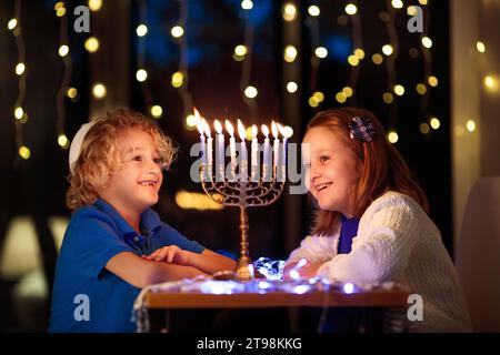 Ragazzi che festeggiano Hanukkah. Festa ebraica delle luci. I bambini accendono candele sulla menorah tradizionale. Ragazzo in kippah con dreidel e Sufganiyah Foto Stock