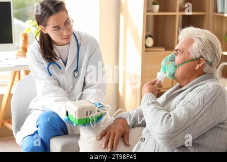 Uomo anziano con nebulizzatore e infermiera a casa Foto Stock