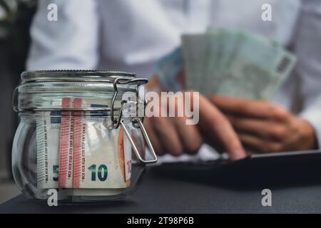 Man Hands conta le spese banconote di contante in euro da barattolo di vetro nel salvadanaio con calcolatrice. Primo piano di mani un uomo d'affari irriconoscibile. Risparmia sul concetto di investimento di budget. Euro finanzia filmati di risparmio Foto Stock