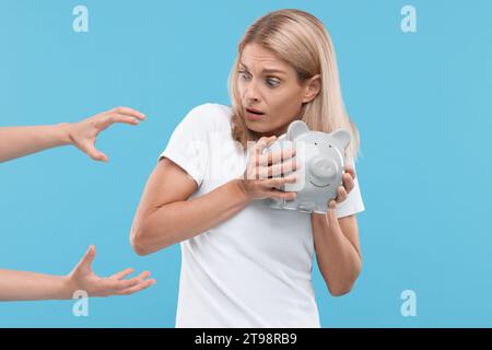 Truffatore che prende salvadanaio da donna spaventata su sfondo azzurro. Attenzione - frode Foto Stock