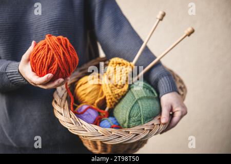 Donna che tiene palla di lana per maglieria o uncinetto. Filato colorato in cestino di vimini Foto Stock