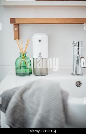 Un moderno interno del bagno con ripiano lavabo bianco con dispenser di sapone cromato e barretta aromatica, ideale per creare un'atmosfera da centro benessere Foto Stock