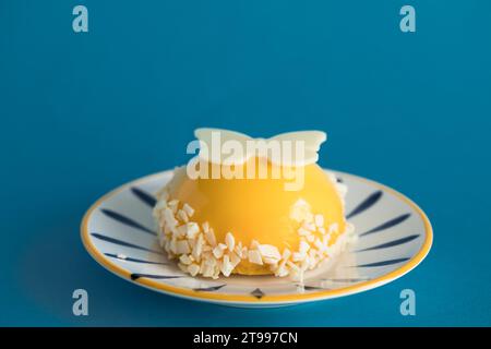 Primo piano Mango Mousse Dome servito su piatto, isolato su sfondo blu Foto Stock