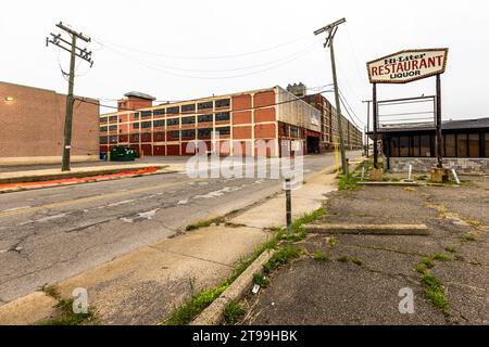 Lo stabilimento Ford di Highland Park, dall'aspetto largamente abbandonato, si estende come un complesso di mattoni lungo la strada. In primo piano, un'insegna per il “Hi-Liter Restaurant Liquor” pubblicizza un esercizio su un lotto adiacente. Lo stabilimento di Highland Park, una città indipendente da Detroit, Michigan, Stati Uniti, ha introdotto la prima linea di montaggio continua al mondo per la Ford Model T il 7 ottobre 1913. Foto Stock