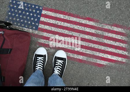 Immigrazione. Uomo con borsa in piedi sull'asfalto vicino alla bandiera degli Stati Uniti, vista dall'alto Foto Stock