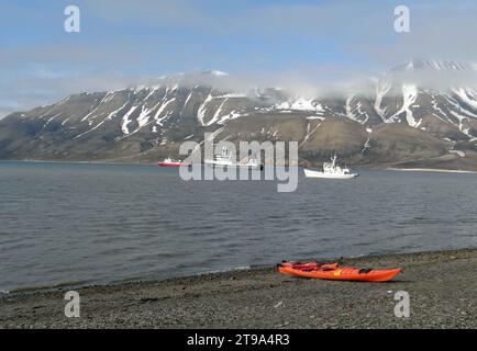 kayak sulla costa. con barche e montagne sullo sfondo, vicino a longyearbyen, spitsbergen, arcipelago delle svalbard, norvegia Foto Stock