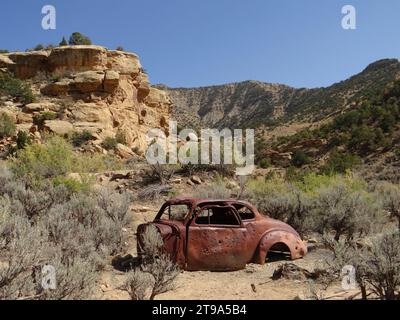 Auto antica arrugginita con fori di proiettile in una giornata di sole accanto a formazioni rocciose erose nella città mineraria fantasma di sego, utah Foto Stock