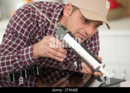 uomo che ripara la cucina con una pistola al silicio Foto Stock