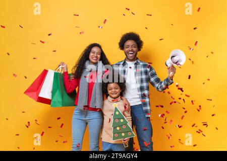 Felice famiglia afro-americana in uno studio per festività natalizie con sfondo giallo e coriandoli Foto Stock