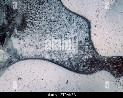 Dall'alto in basso sopra la vista di un laghetto ghiacciato con consistenza cristallina ricoperta di neve, sfondo invernale naturale Foto Stock