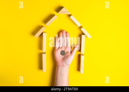 Vista dall'alto della mano del bambino da vicino gli edifici che mostrano i soldi della macina, la casa, la capanna di legno Foto Stock