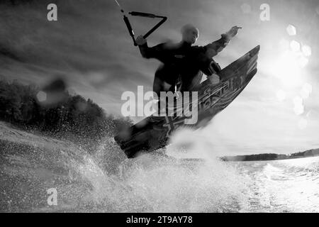 Immagine in bianco e nero ad angolo ridotto di un wakeboarder maschio che fa un 360 sopra la fotocamera. Foto Stock