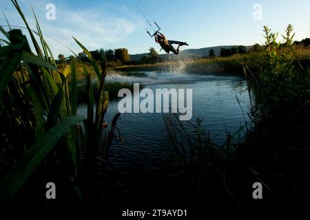 Sull'uomo si vedeva il kiteboarding nella palude attraverso le canne in bella luce. Foto Stock